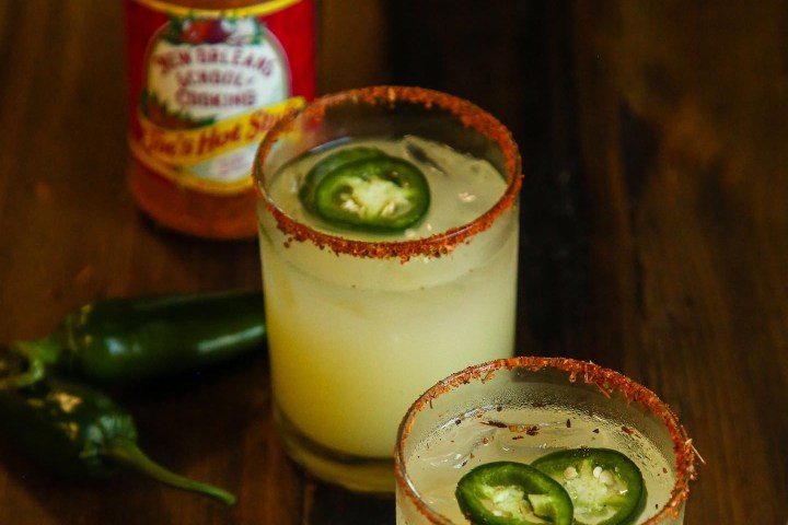 Two spicy cocktails with jalapeño slices and chili powder rim, surrounded by spices and jalapeños.