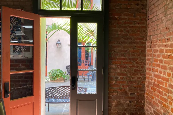 Open red door with glass panels, leading to courtyard with chairs and plants.