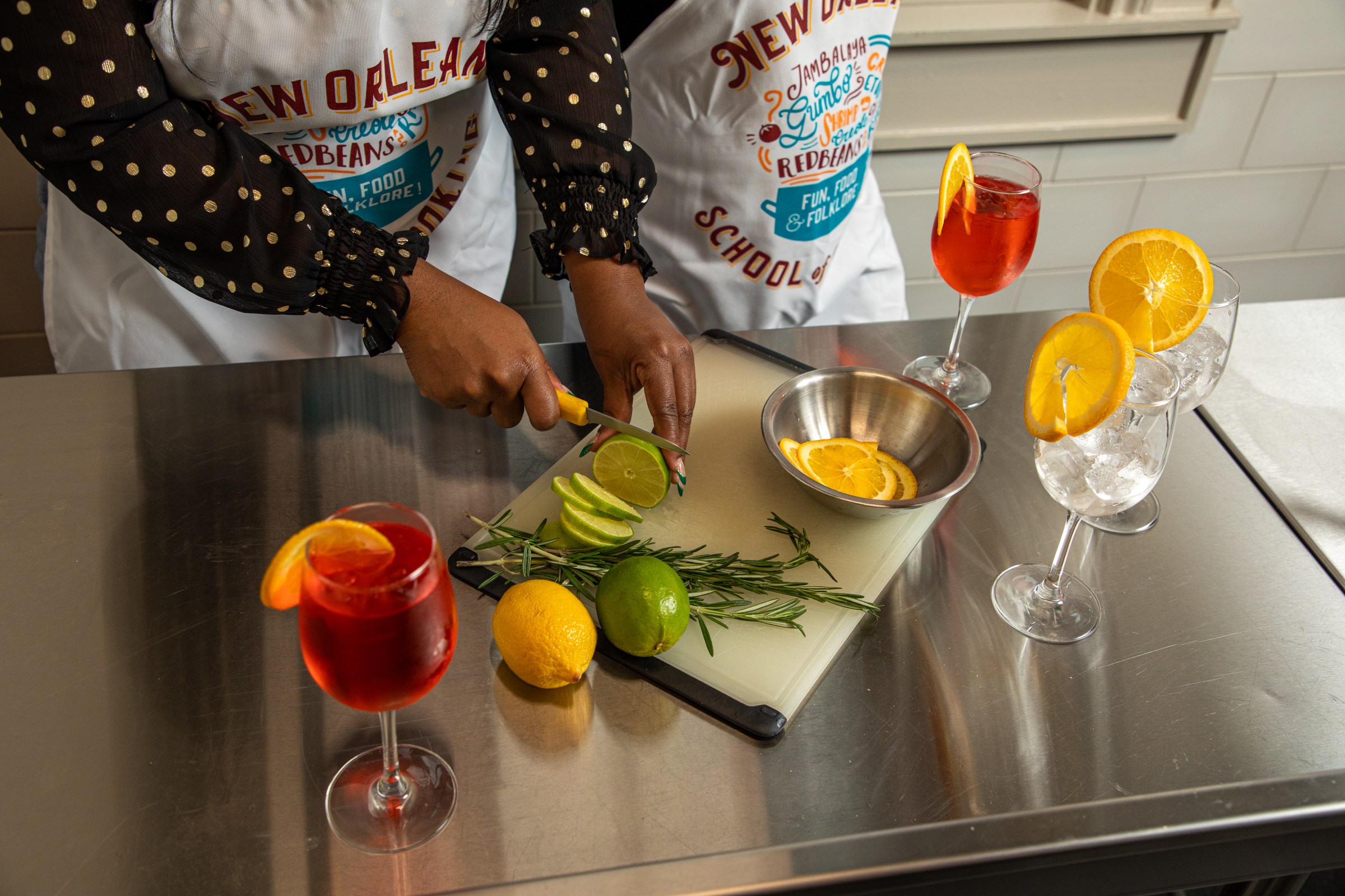 NOSOC_Jan2025-290 Two people are slicing lime garnishes for Aperol Spritz during our new cocktail-making class at the New Orleans School of Cooking.