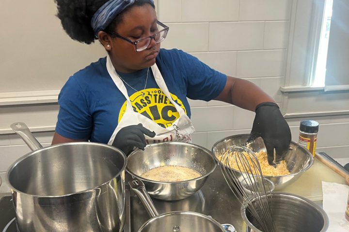 Person cooking with various pots on a stove, wearing a blue shirt and an apron.