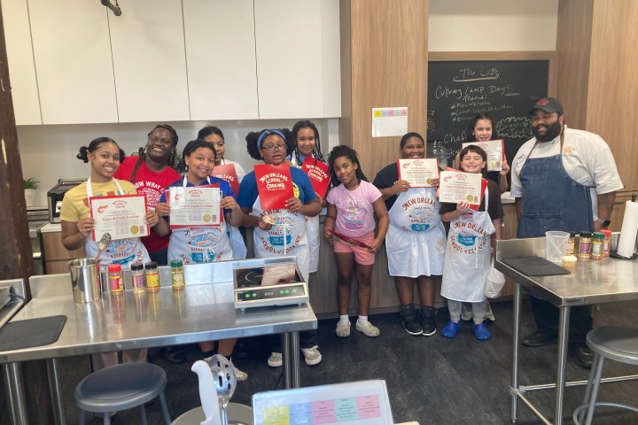 Group of kids in aprons holding certificates in a kitchen with a chef.