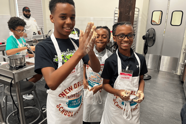 Children in aprons smiling while handling dough in a cooking class setting.