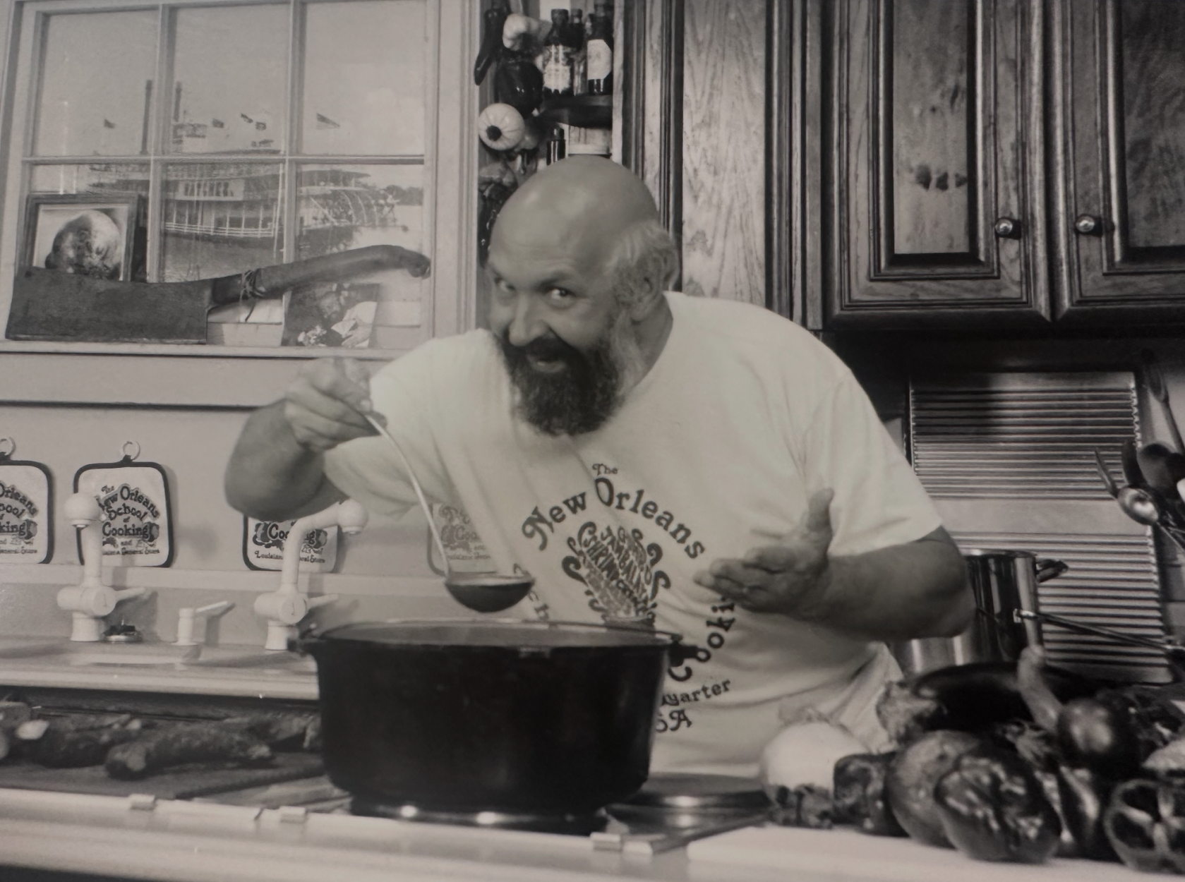Joe Cahn, cooking and smiling, holding a ladle over a pot in a kitchen.