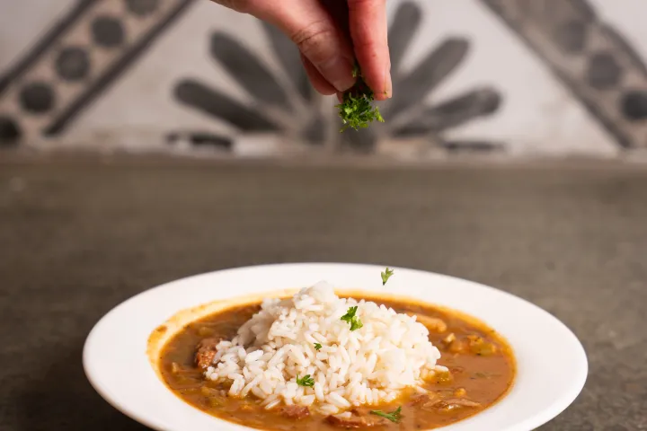 Hand garnishing rice and curry with herbs on a plate.